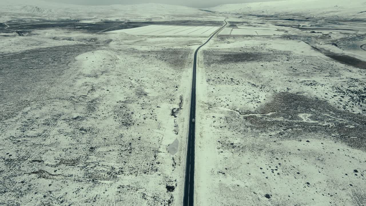Vista aerea di un'auto che percorre una strada innevata attraverso un desolato paesaggio invernale.