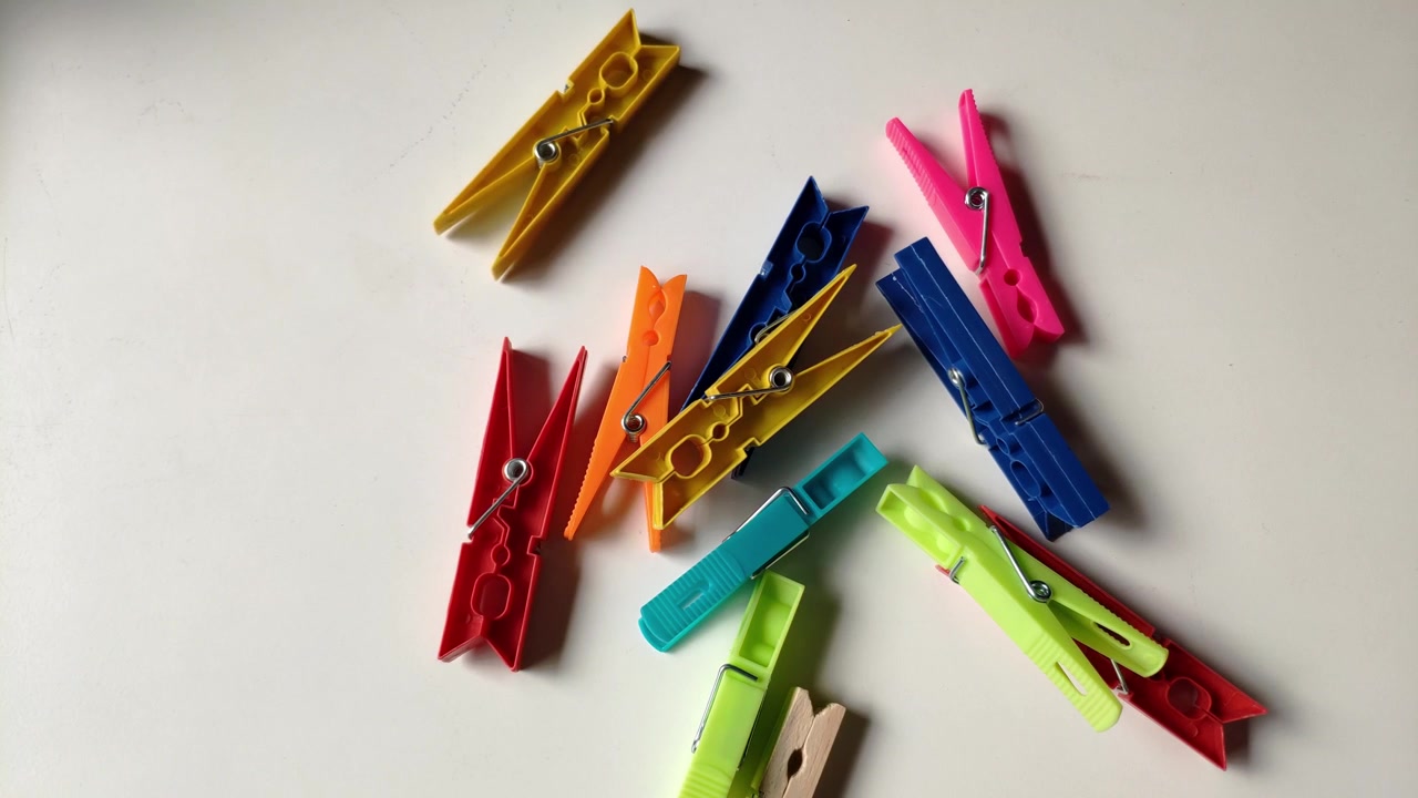 Mano che ordina mollette colorate di plastica e legno su una superficie di tavolo bianca.