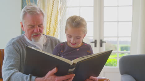 Grandfather-And-Granddaughter-Looking-Through-Photo-Album-In-Lounge-At-Home-Together