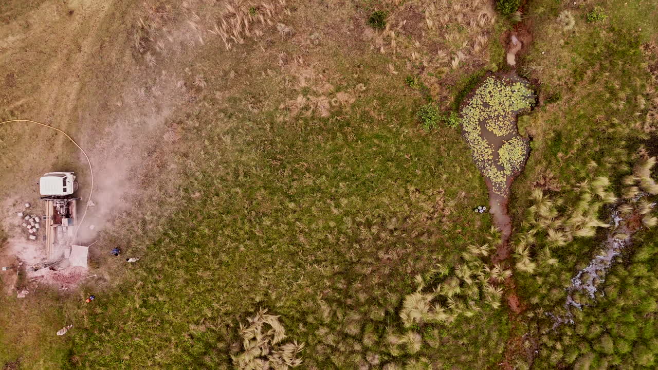 сельская операция по бурению воды в травяном поле с близлежащей зеленью и прудом, взгляд с воздуха