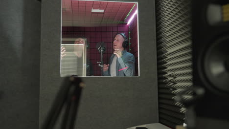 two men in a red soundproof room sing passionately. one wears a black cap and shirt, and the other is dressed in a blue shirt and white inner shirt. both are engaged in a focused, musical performance