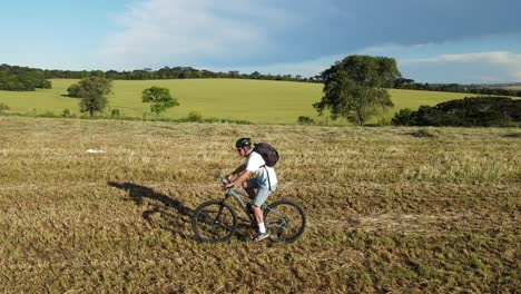 Biker-pedaling-in-a-field-with-rolls-of-hay-silage,-drone-view