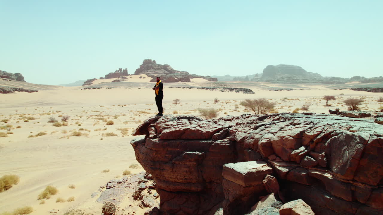알제리의 djanet에 있는 황량한 사막을 보기 위해 바위 가장자리까지 고 있는 남자