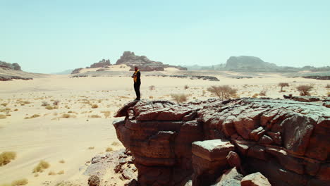 un tipo caminando hasta el borde de una roca para mirar el desierto estéril en djanet, argelia.