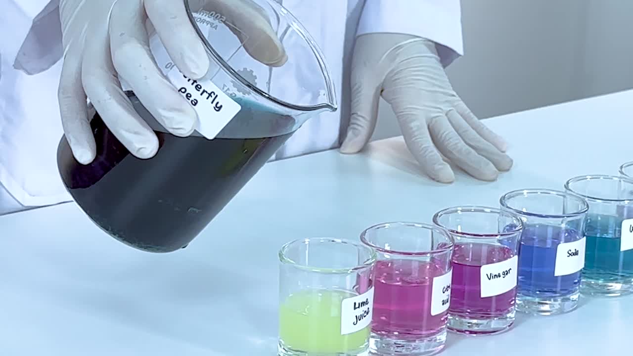 Gloved hands pour dark liquid into beakers, causing vibrant color changes in a laboratory setting.