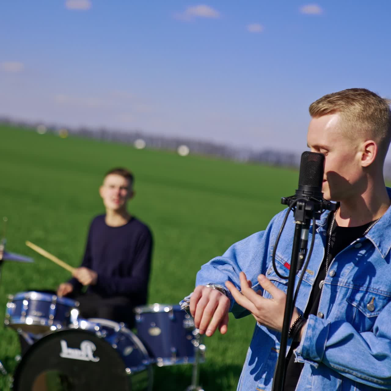Boys band singing and playing music open air in the green field. Lead singer performing song at the microphone stand