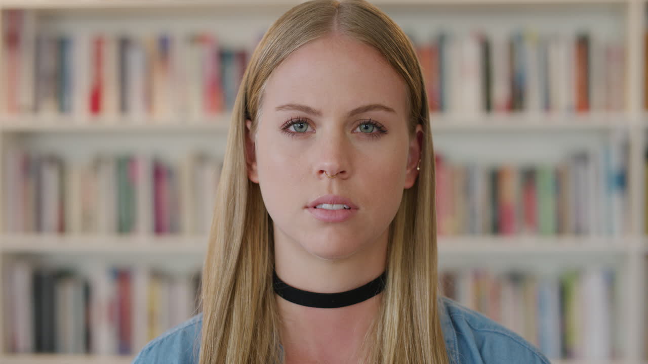 retrato joven hermosa mujer rubia estudiante buscando serio calma caucásica mujer cámara lenta en la biblioteca estantería fondo