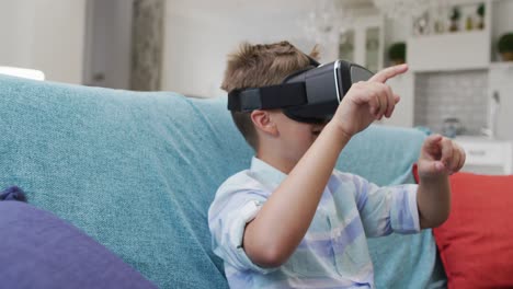 niño caucásico feliz en casa, sentado en el sofá con auriculares vr y sonriendo