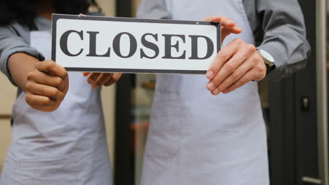 close-up view of caucasian waiter and african waitress hands holding a signboard closed" outside of coffee shop"