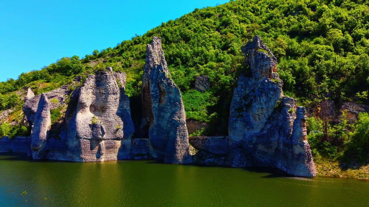 Kalkstenspelare vid flodkant, Bulgarien. Närperspektiv av naturliga stenformationer som reser sig från vattenytan nära en skogklädd strand