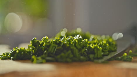 close-shot-of-fresh-chopped-chives-laying-on-a-wooden-cutting-board,-then-water-is-sprayed-on-it