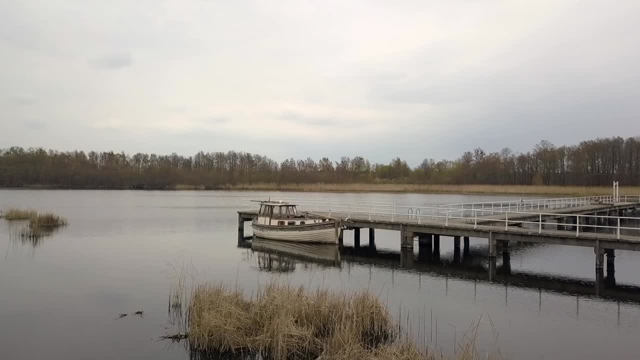 impresionante vuelo aéreo volando hacia adelante con un dron disparado sobre el agua a un barco de pesca en un embarcadero al atardecer de primavera en un lago en una ubicación perfecta en brandeburgo, alemania