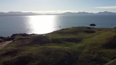 vista aérea del paisaje de la isla galesa de ynys llanddwyn con el océano brillante y la cordillera nebulosa de snowdonia a través del horizonte del amanecer