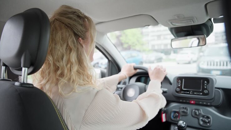 Vista dal sedile posteriore di una donna d'affari bionda che avvia il motore e manovra il suo veicolo