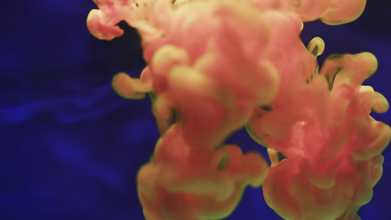 Video al rallentatore di inchiostro acquerello rosa e giallo che si mescola nell'acqua su sfondo blu