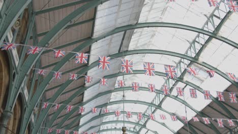 Union-Jack-Flaggen-Schmücken-Den-Covent-Garden-Market-Mit-Touristen-In-London,-Großbritannien-2