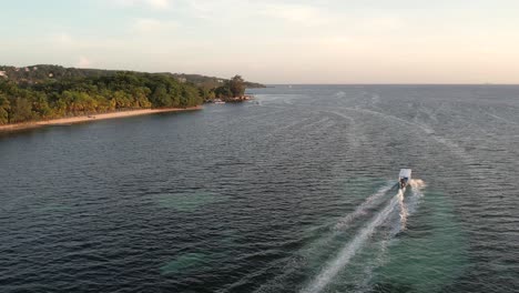 White-speed-boat-on-clear-turquoise-sea-surface-with-coral-reef-moving-towards-an-island