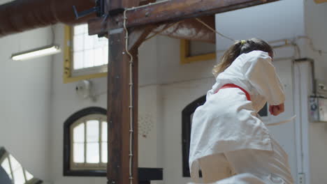 front view of focused girl in kimono practicing karate in gym