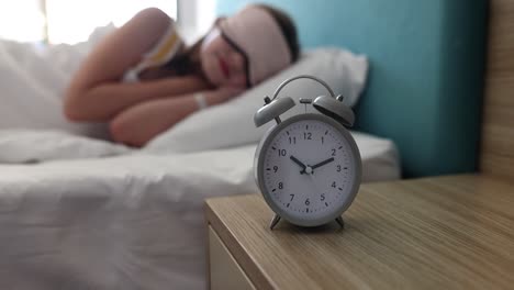 alarm clock on nightstand with person sleeping in bed