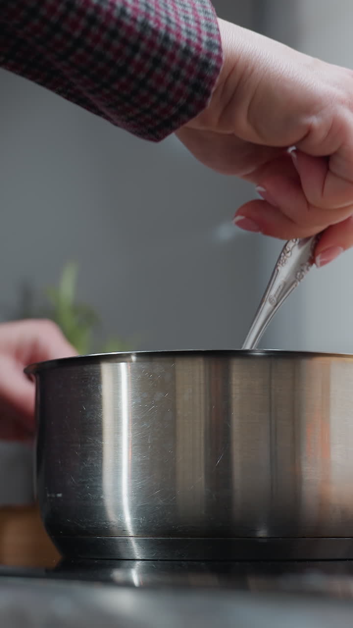 primer plano de sopa agitada a mano en una olla de acero inoxidable en la estufa, con ropa a cuadros, vista parcial de una bandeja de madera con ingredientes en la encimera, entorno de cocina moderno
