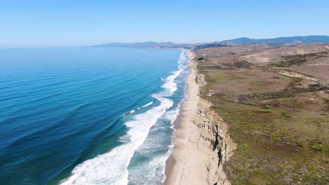 Aerial-video-of-Pescadero-Coast's-shore,-along-with-green-mountains,-and-a-road-with-cars-passing-by-in-San-Mateo-California