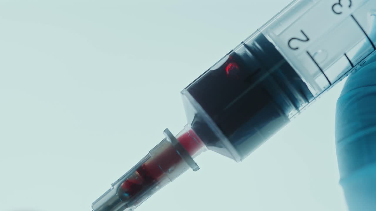 Gloved Hand Drawing Blood with Syringe against Illuminated Background