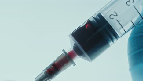 gloved hand drawing blood with syringe against illuminated background