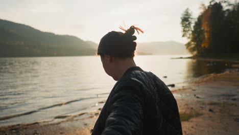 wife holds husband hand on riverbank at sunset. romance blossoms between young couple during sharing holidays among rural landscape. optimistic moments of life