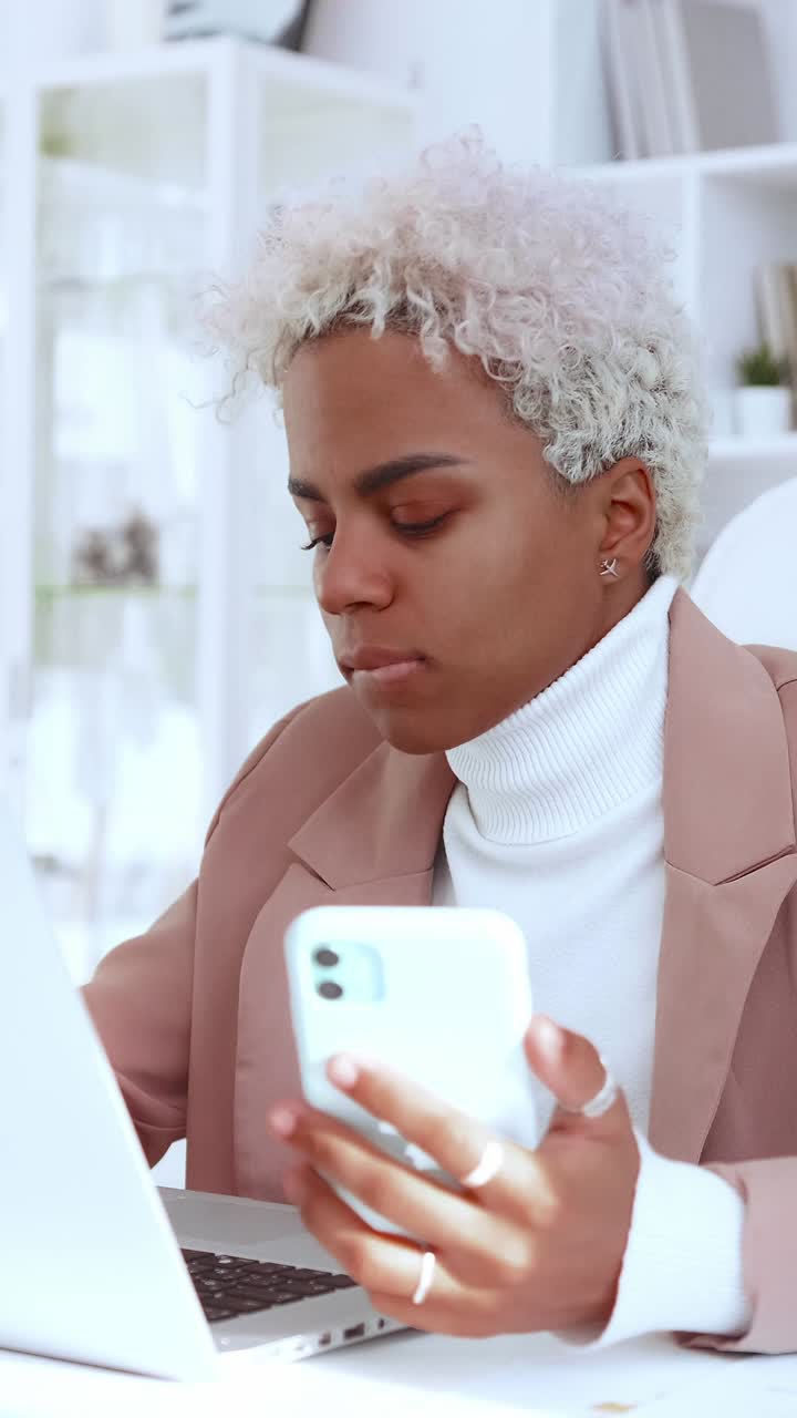 Focused individual working on laptop while holding a smartphone in office