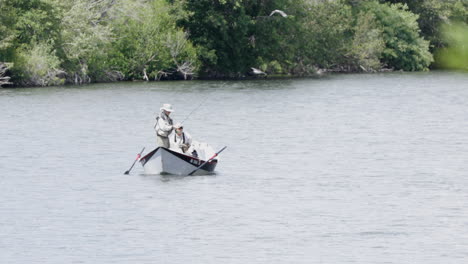 wide shot of two men fishing on river, birds flying overhead. static shot.