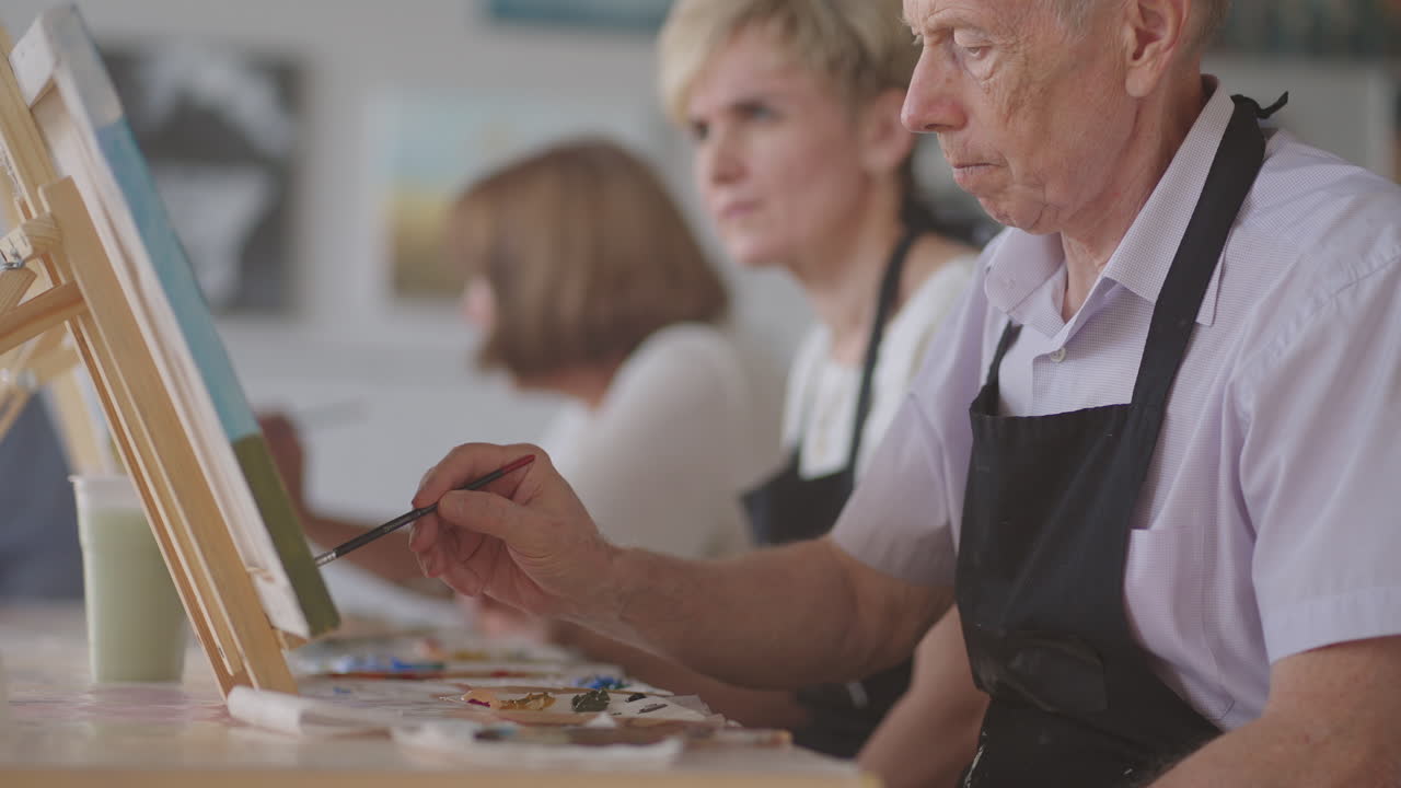 Senior man with friends draws a picture. The old man's club is having fun and painting together.
