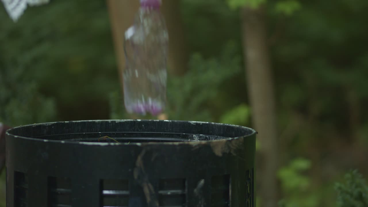 Hand dropping plastic bottle into trash bin in green park