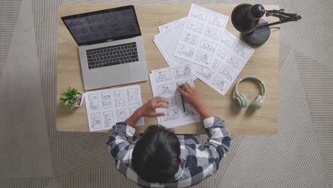 vista superior de un artista masculino asiático que tiene dolor de cabeza mientras dibuja un guión gráfico para la película en la mesa con una computadora portátil y auriculares en el estudio