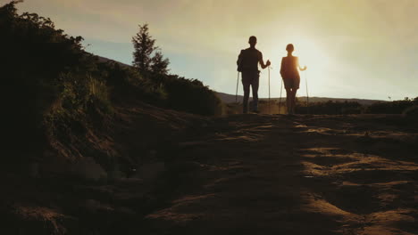 A-Couple-Of-Tourists-With-Backpacks-And-Trekking-Sticks-Descend-Down-The-Montaña-In-The-Sun-Beautif