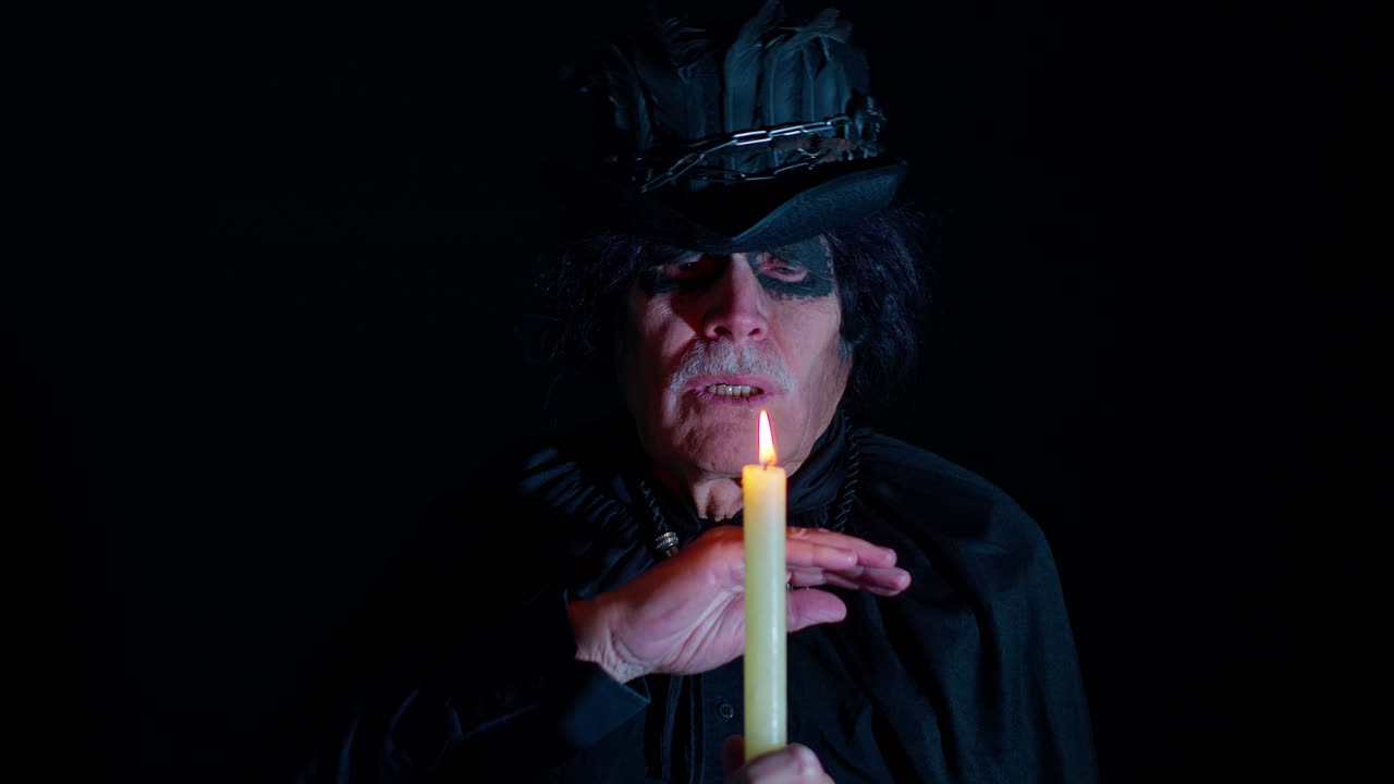 hombre maduro y siniestro en disfraz de carnaval de halloween hechicero haciendo rituales mágicos con velas