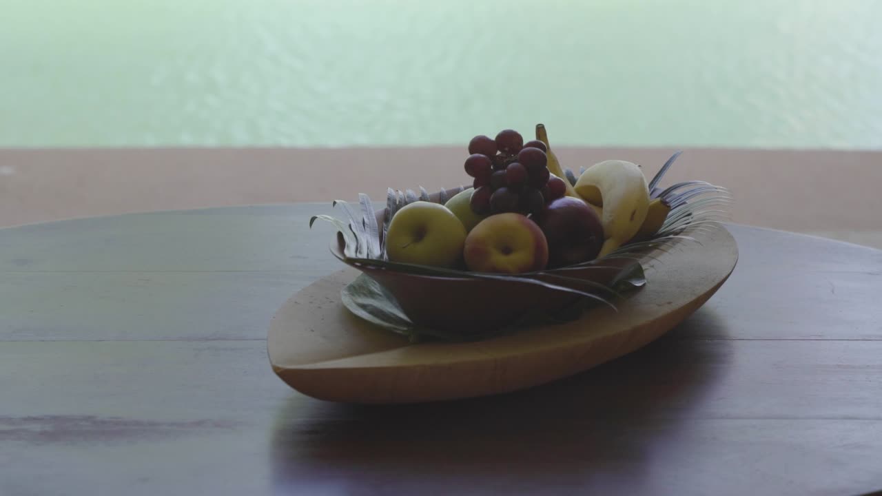 Close up of a tropical decorated tray of fruit being put down on a table with a pool in the background