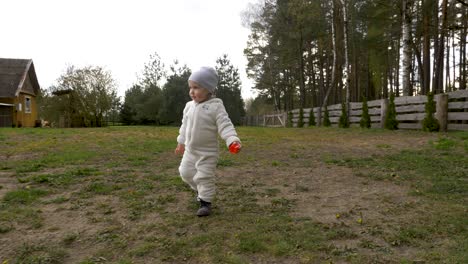 Toddler-girl-wearing-warm-clothes,-walks-in-the-yard-with-her-toys