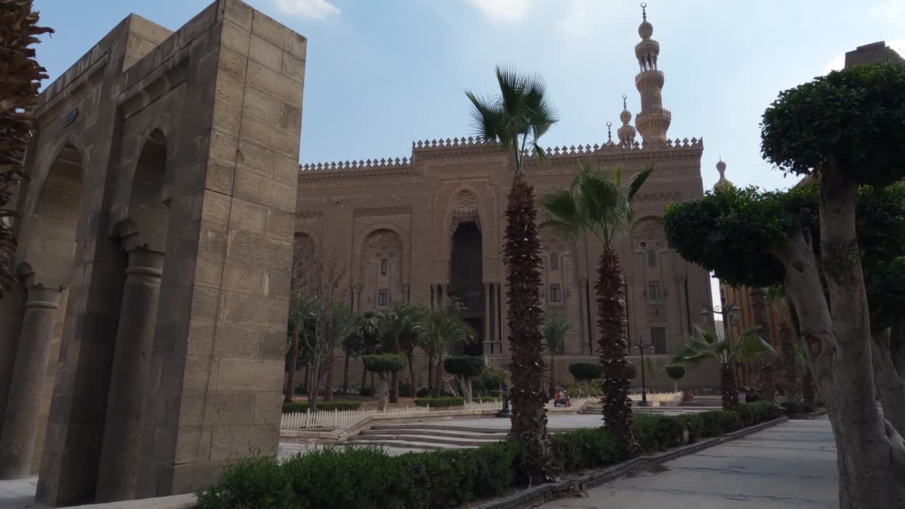 exterior de la mezquita de la madrasa del sultán hassan con palmeras y turistas de pie. el cairo, egipto.