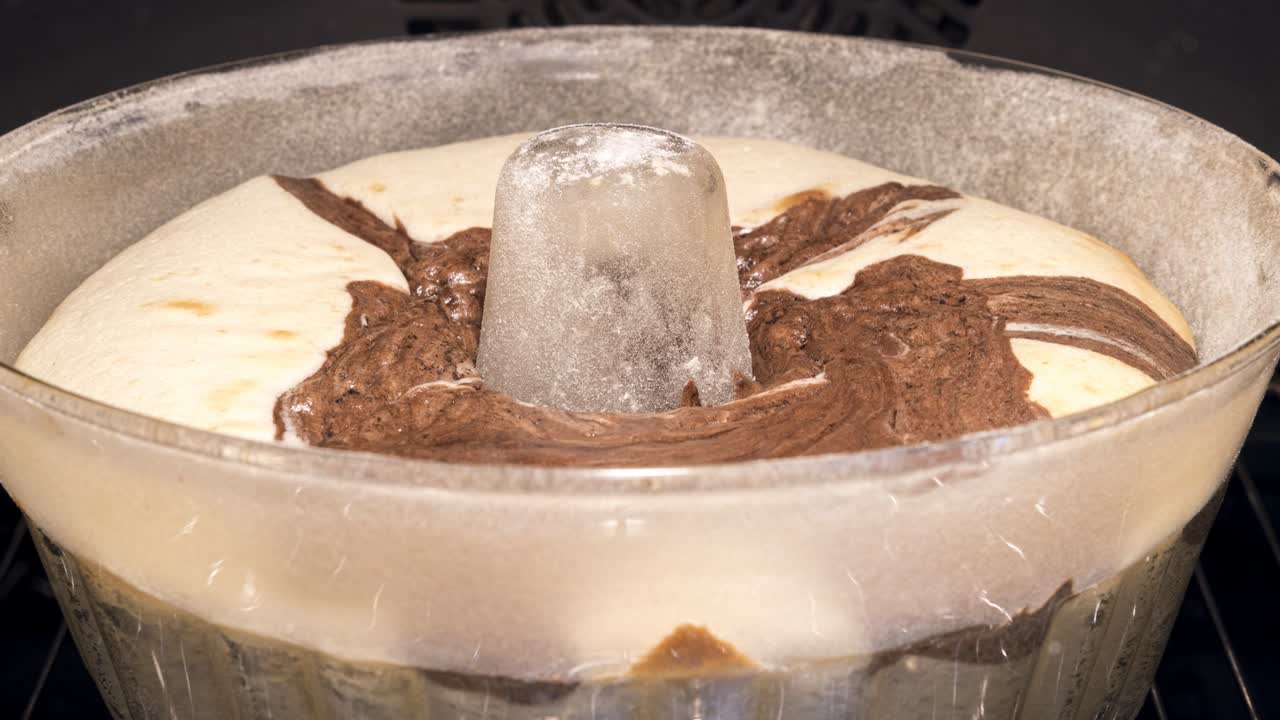 Baking of a traditional and delicious bundt cake in a glass mold. Pastry slowly rising up above the edge of the form. Homemade sponge marble cake. Front view into an oven, time lapse video