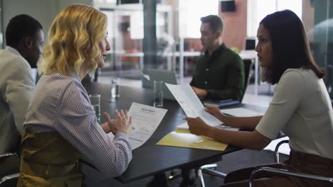 diverse group of business colleagues wearing talking in meeting room holding documents using laptop