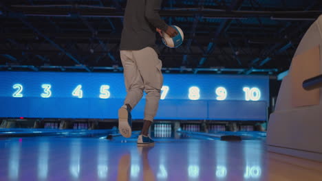 the camera follows one black man throwing a bowling ball on the playing track and jumping around rejoicing in the downed pins. one man bowling in slow motion