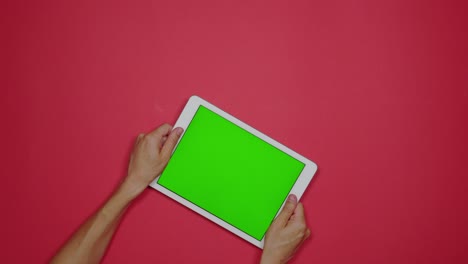 manos sosteniendo una tableta con pantalla verde sobre una placa plana roja