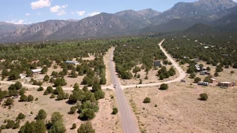 White-SUV-leaving-the-Colorado-Rocky-Mountains-with-desert-shrubs-on-both-sides,-aerial-front-view