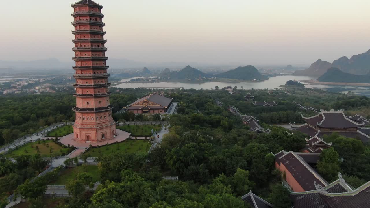 vista aérea de drones en vietnam volando sobre un área de templo budista, pagoda y estatua de buda llena de árboles verdes frente a un río serpiente en ninh binh al atardecer