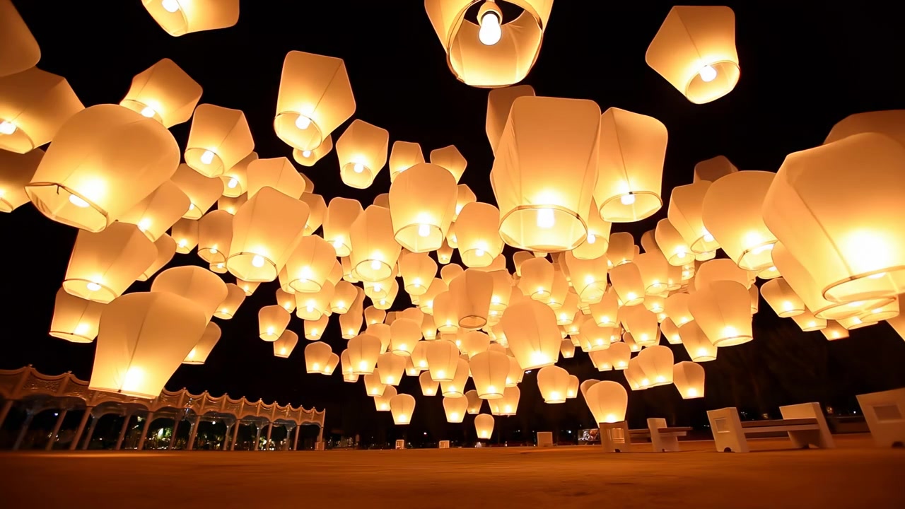Tallrike papirhimmelballonger svever over et mørkt åpent rom, glødende med varme ravgule flammer mot en svart nattehimmel, noe som skaper en rolig festivalstemning, myk kontrast og lagdelt dybde.