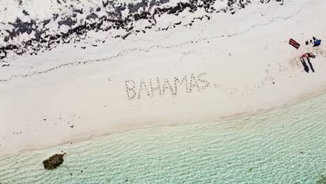 a couple wrote "bahamas" on the beach with shells