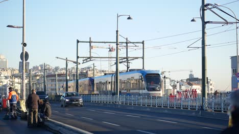 a city scene with a tram, cars, and people on a bridge