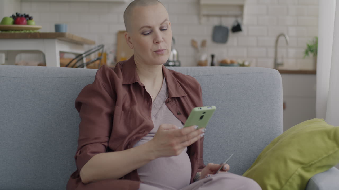 Pregnant Woman Using Phone and Credit Card at Home