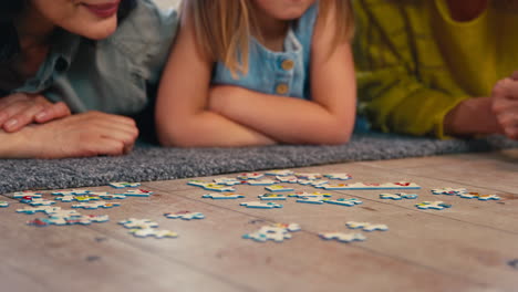 Nahaufnahme-Einer-Gleichgeschlechtlichen-Familie-Mit-Zwei-Reifen-Müttern-Und-Ihrer-Tochter,-Die-Auf-Dem-Boden-Liegen-Und-Puzzle-Machen