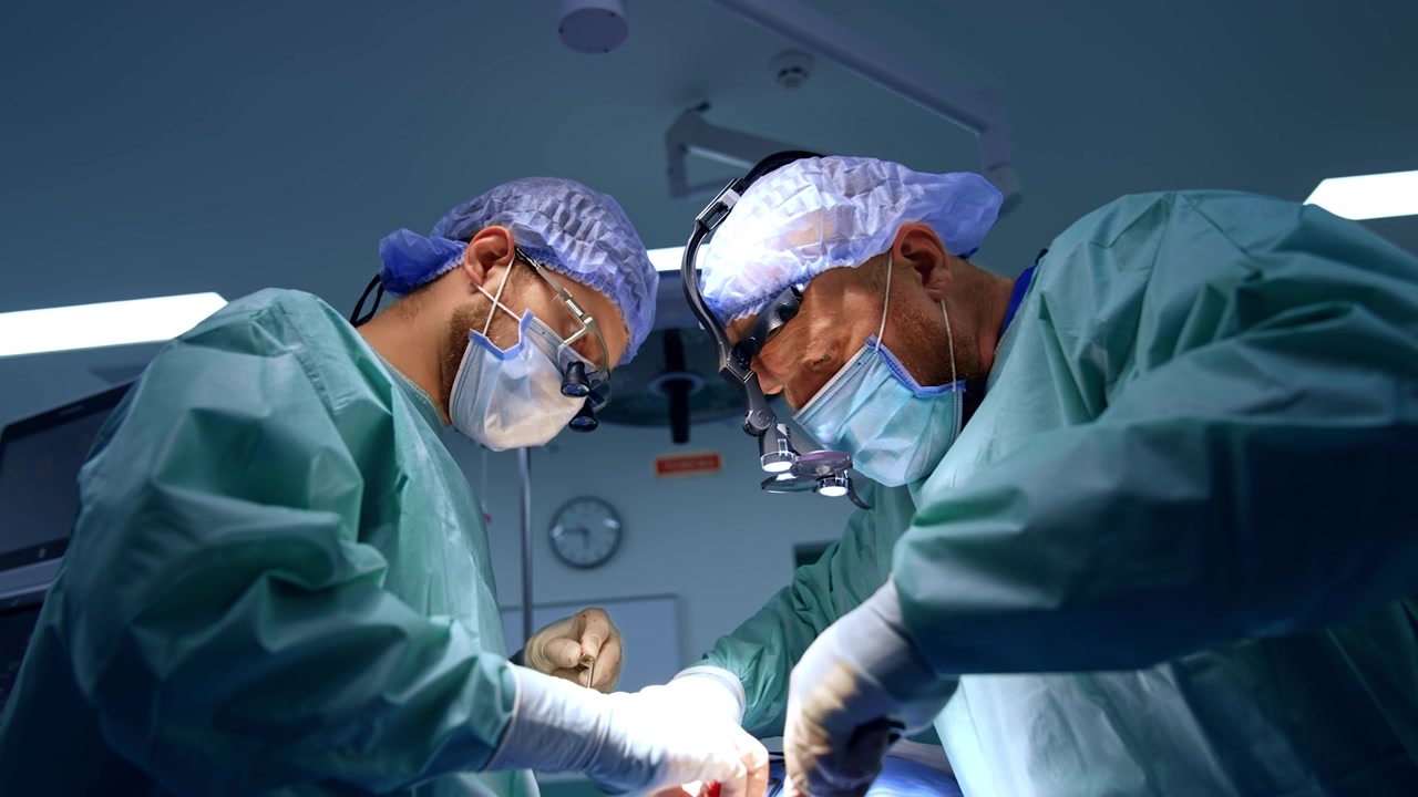 Due chirurghi collaborano in un intervento di chirurgia maxillo-facciale. Medici attenti con occhialini chirurgici usano attentamente gli strumenti. Vista dal basso.